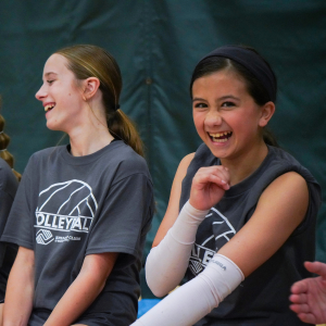 two players laugh together on bench Two Boys & Girls Clubs of Whatcom County volleyball players celebrate a play by high-fiving each other