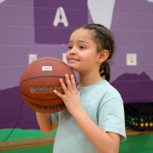 kid holding basketball and smiling A girl smiles as she gets ready to throw a basketball